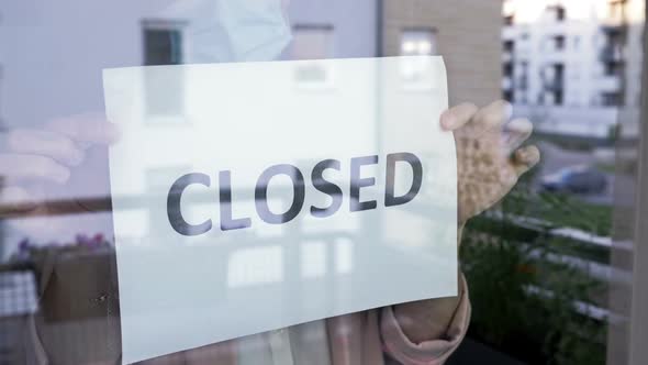 Woman in a Medical Mask Fastens the CLOSED Sign at the Glass Door. Shutdown of Restaurants, Shopping