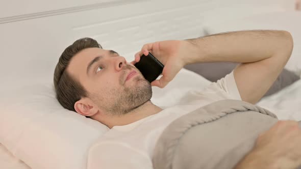 Young Man Talking on Smartphone Laying in Bed