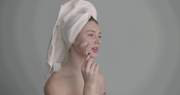 Woman Using Jade Roller on Her Face Over Grey Background