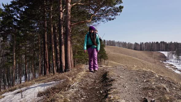 A Young Mother Carries Her Child in a Backpack Along a Forest Trail in the Mountains in Spring