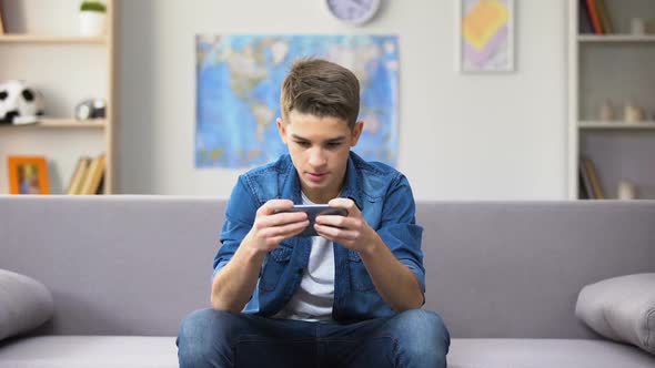 Gadget Addicted Caucasian Teenager Playing Game on Smartphone, Wasting Time