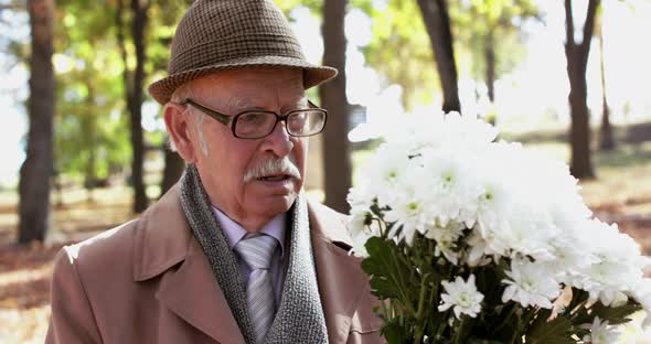 Close Elegant Senior Man with Bouquet of Flowers Walks on Romantic Meet in Park