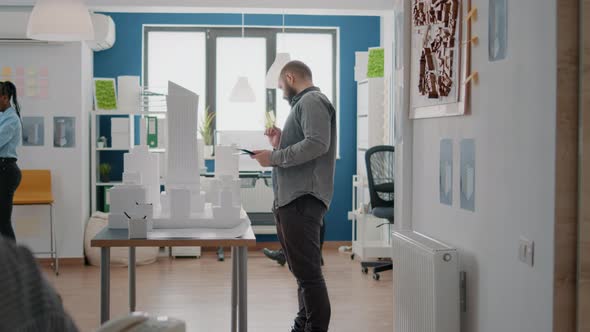 Architect Using Digital Tablet and Building Model to Design Blueprints Plans for Construction