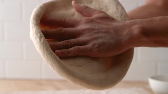 Camera follows man’s hands flattening a dough. Slow Motion.