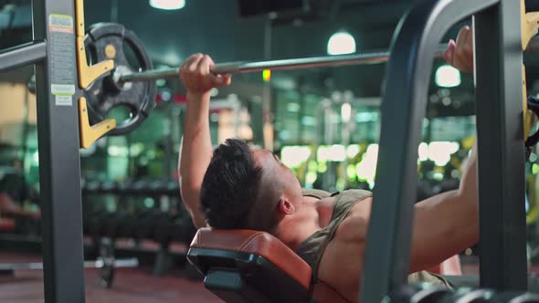Asian sportsman workout exercise by slowly lift up weight machine or barbell in fitness stadium.