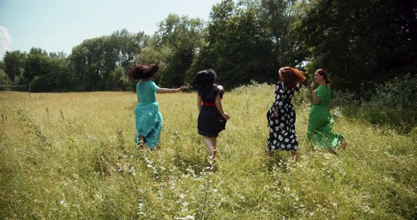 Four Fashionable Girls Running On A Green Meadow