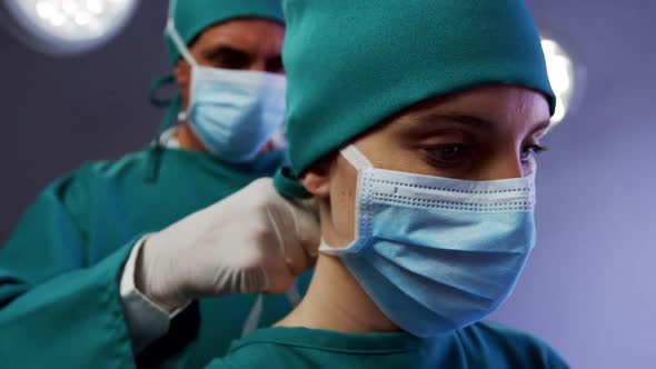 Surgeon helping a nurse in tying surgical mask in operation room