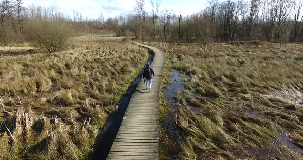 Aerial view of a guy walking alone on a wooden pathway in a meadow in the fall.