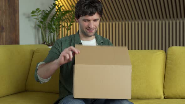 A Human Customer Receives a Parcel Open Cardboard Box While Sitting on a Yellow Sofa at Home