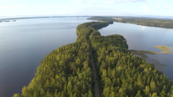 Aerial shot of following a car driving on road that goes through island surrounded by a lake in Finl