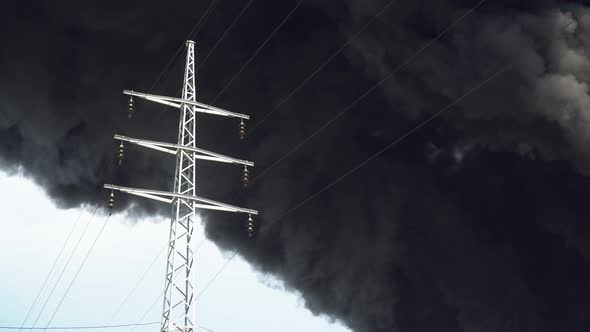 An Electric Tower Stands Against a Background of Black Smoke. A Big Chemical Fire at a Factory