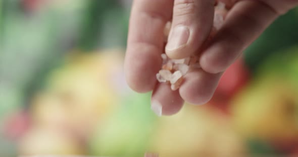 Fingers Salting With Coarse Pink Himalayan Salt And Green Vegetables On The Background