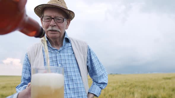 Senior Farmer Clinking Beer Mugs with Friend at Camera in a Barley Field