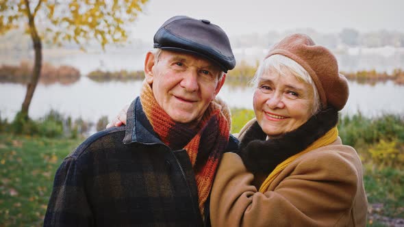 Retired Pair Grandparents are Smiling and Looking at you with Love Posing at City Park Against a