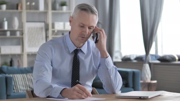 Gray Hair Businessman Talking on Phone and Writing Information