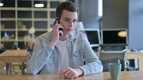 Cheerful Young Designer Talking on Smartphone in Office