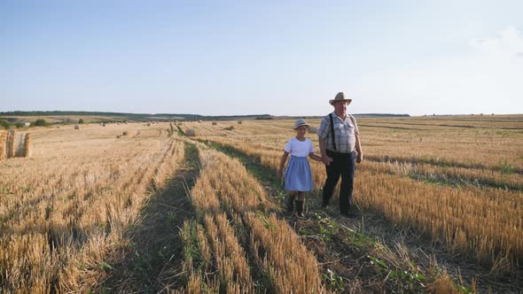 Grandfather and Granddaughter Walking Across the Field with Haystacks