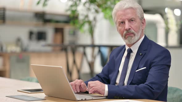 Serious Senior Old Businessman with Laptop Looking at the Camera 