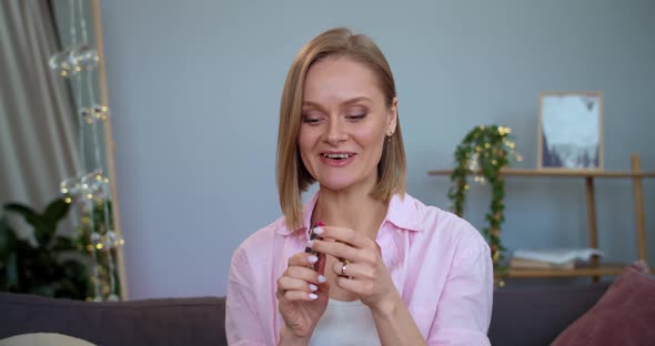 Cheerful Female Vloger Presenting To Camera Lipstick and Talking While Sitting on Couch at Home