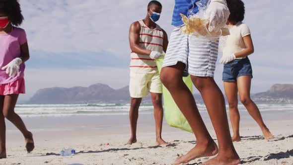 African american parents with two children wearing face masks collecting rubbish from the beach