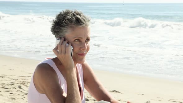 Senior woman using cell phone on beach