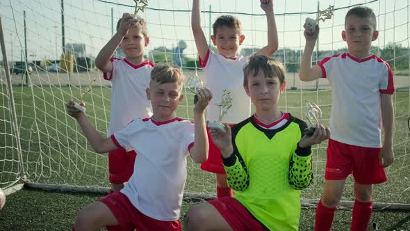 Junior Schoolboys in Football Uniform Hold Trophies