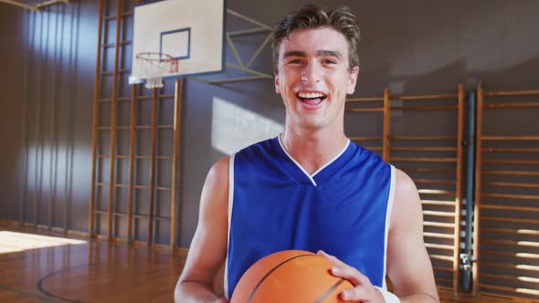 Portrait of caucasian male basketball player holding ball and smiling