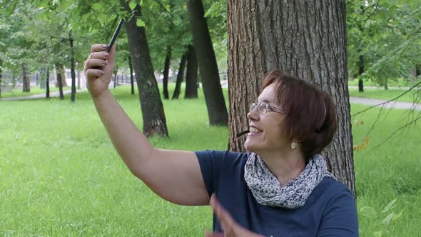 Happy Smiling Senior Woman Having Video Call While Sitting on the Grass in City Park