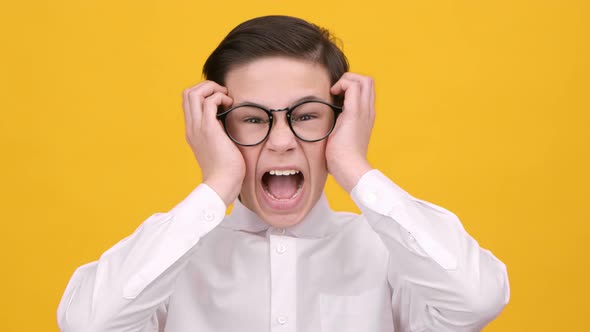 Crazy Schoolboy Shouting In Anger Touching Head Over Yellow Background