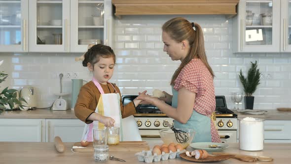 Mom Wipes the Baby's Hands and Dusts Off the Flour While Cooking in the Kitchen. My Daughter Helps