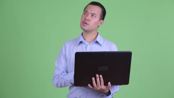 Happy Asian Businessman Thinking While Using Laptop