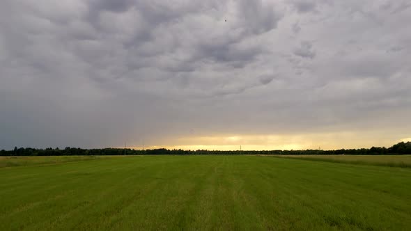 Closeup flight over green summer field in Munich, Germany. Dramatic sky with storm clouds at sunset.