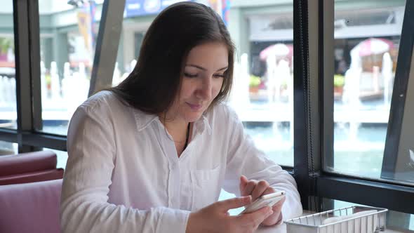 Brunette Woman with a Phone at a Table in a Cafe