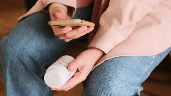 Woman checks pills medicines using her smartphone. Holding a bottle of pills instructions for use