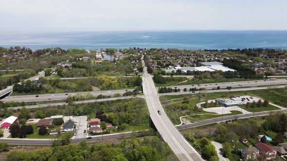 Aerial pan shot showing bridge road following over asphalt highway towards Lake Ontario during summe