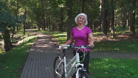 Elderly sportive woman is engaged in outdoor cycling in the forest.