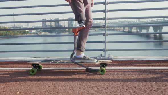 Man with Leg Prosthesis Skateboards Along City Embankment