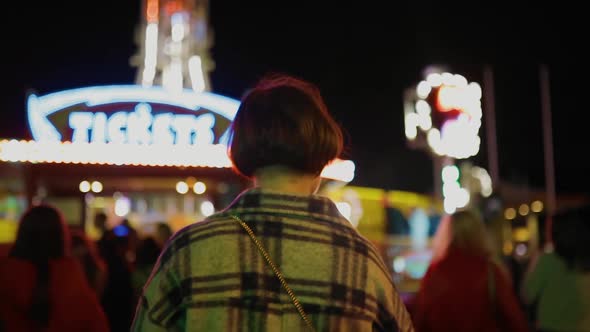 Woman in Checked Coat Walks Forward at Amusement Park