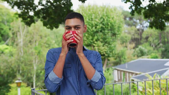 Portrait of mixed race man standing in garden drinking a mug of coffee and smiling
