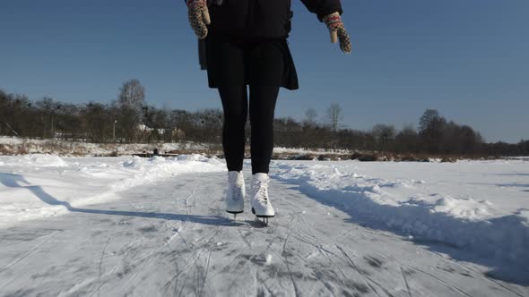 Romantic young woman in skirt and white figure skates is skating on frozen river