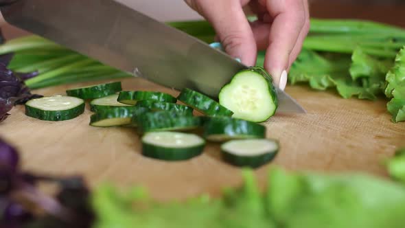 Closeup of a Woman Cutting a Fresh Cucumber on a Wooden Cutting Board