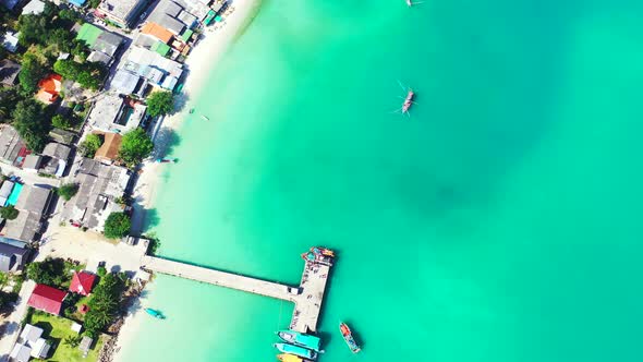 Sandy beach and pier over the turquoise seawater. Boats floating in the calm lagoon with luxury reso