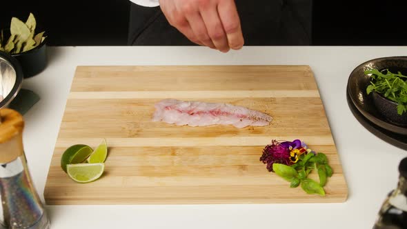 Professional Chef Adding Spice on Raw White Fish Fillet on Cutting Board Closeup Thin Slice