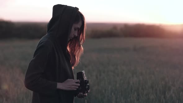 Female Stands in Field with Vintage Camera on Background Sunset with Sun Glare