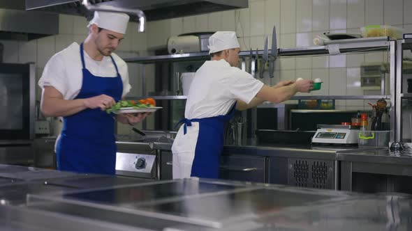 Male Cook with Vegetables on Plate Passing Colleague Examining Mushrooms in Slow Motion Leaving