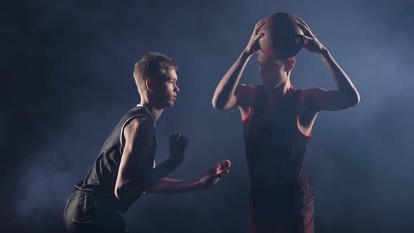 Two Young Athletes Practice Basketball in a Dark Smoky Studio Under the Spotlight