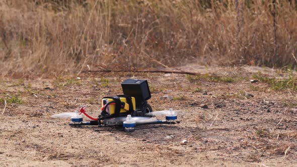FPV Racing Drone Takes Off From a Dirt Surface Raising Dust and Stones