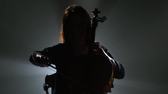 Silhouette of a Musician with a Cello in a Dark Studio . Black Smoke Background