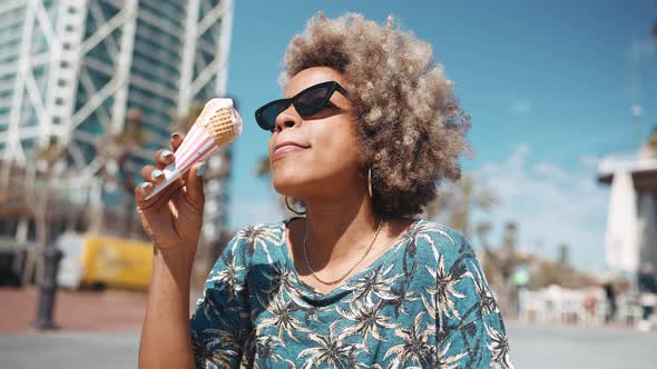 Happy African grey haired woman eating ice cream while sitting on the bench