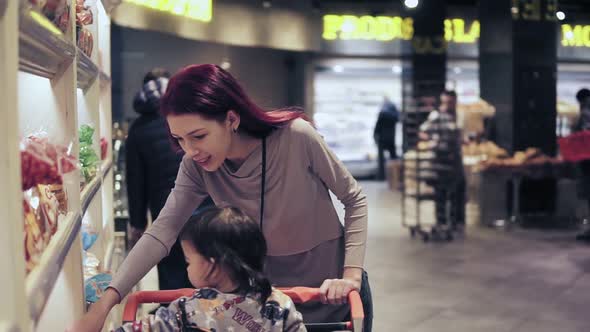 Young Woman with Her Toddler Son is Picking Out Bread at Local Grocery Store